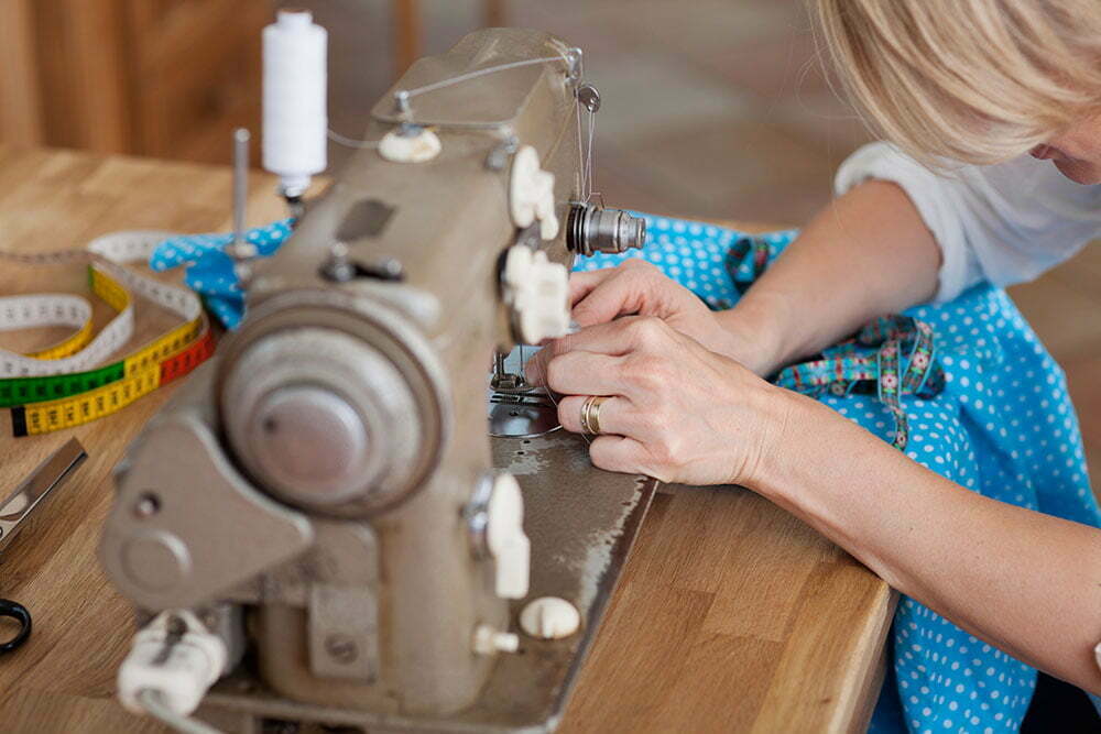 A woman sews blue fabric with machine